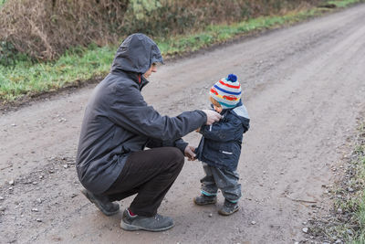 Side view of grandfather with granddaughter crouching on dirt road