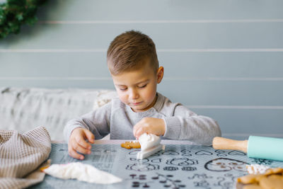 A beautiful baby boy sits on the kitchen table and helps his mother bake and decorate cookies