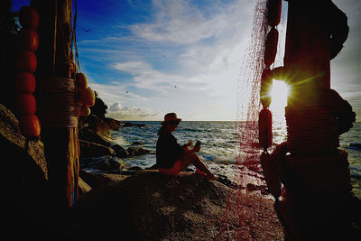 Man sitting on beach looking at sea against sky