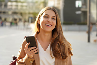 Portrait of cheerful multi ethnic female in trendy wear spending time on street using smartphone