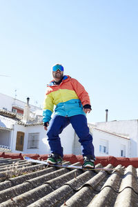 Boy with ski goggles snowboarding on the roof and looking at the camera