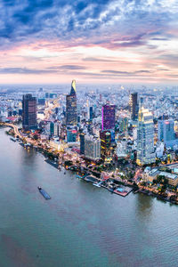 Aerial view of cityscape by river against cloudy sky during sunset