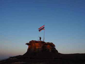 Flag on rock formation against clear blue sky