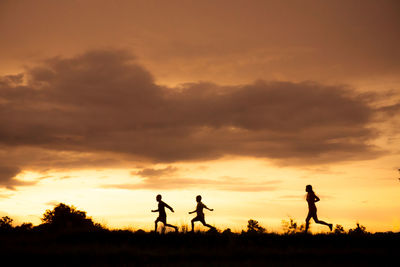 Silhouette people running on field against sky during sunset