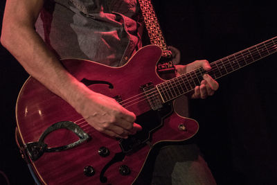 Midsection of man playing guitar against black background