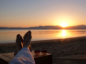 Low section of woman relaxing on beach during sunset