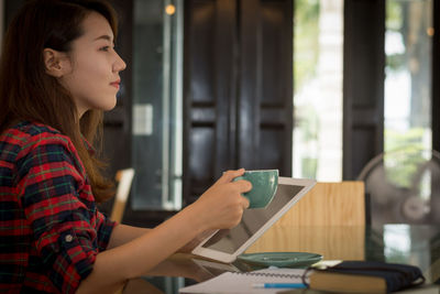 Side view of young woman using phone while sitting on table