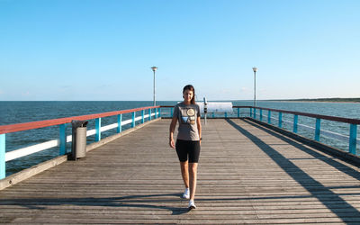 Rear view of man standing on pier over sea against sky