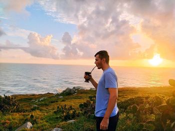 Side view of man standing against sea during sunset