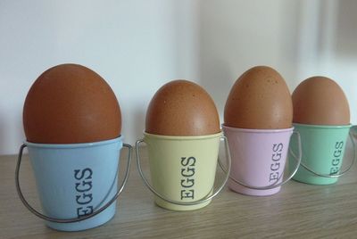 Eggs in pastel coloured bucket-style egg cups on a wooden shelf