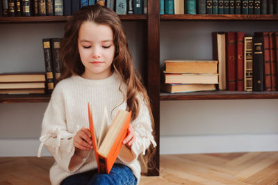 Cute girl opening book while sitting at home