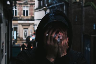 Close-up of man smoking cigarette while covering face with hands