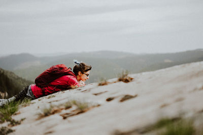 Side view of woman lying on mountain against sky