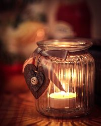 Close-up of heart shape pendant hanging on jar with burning candle