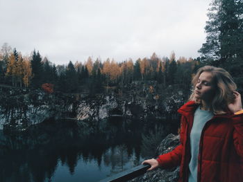 Woman standing by lake in forest against sky during winter