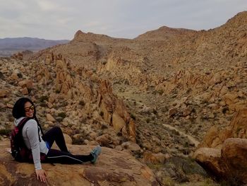 Man sitting on rock by mountains against sky