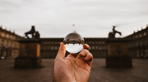 Cropped hand of person holding crystal ball against built structure