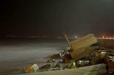 Illuminated rocks by sea against sky at night