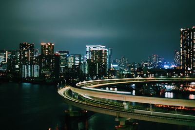 Illuminated bridge and buildings against sky at night