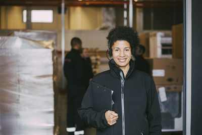 Smiling female entrepreneur with clipboard at warehouse