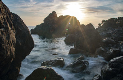 Rocks in sea against sky during sunset