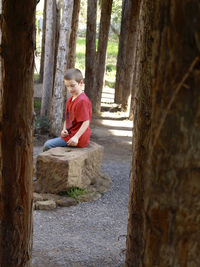 Side view of boy sitting on rock amidst trees at santa barbara botanic garden