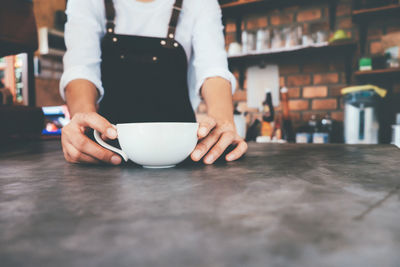 Midsection of barista serving coffee at table in cafe