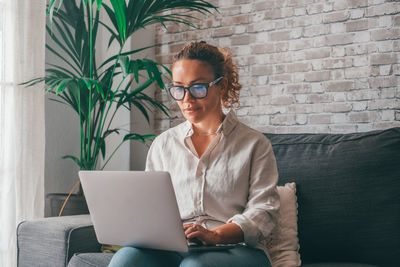 Young woman using laptop while sitting on sofa at home