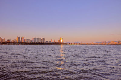 Scenic view of sea by buildings against sky during sunset