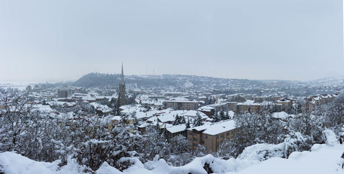 Snow covered houses by city against sky