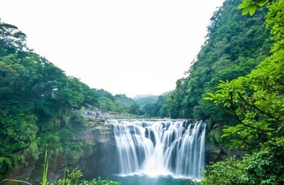 Scenic view of waterfall in forest against clear sky