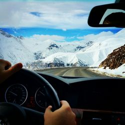 Cropped image of person driving car on road towards snow covered landscape