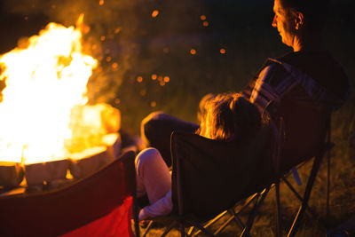 Dad and daughter sit at night by the fire in the open air in the summer in nature. family camping