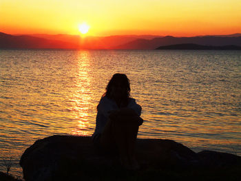 Man sitting on beach against orange sky