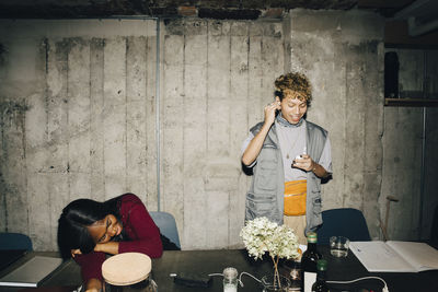 Smiling entrepreneur wearing in-ear headphones while female coworker sleeping at table in office