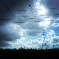 Low angle view of electricity pylon against cloudy sky