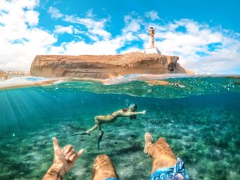 Low section of man showing shaka sign while swimming with woman in sea