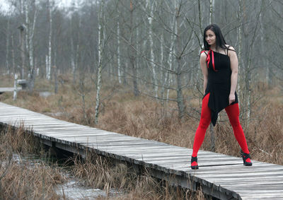 Portrait of woman standing on footbridge against bare trees