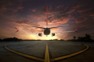 Airplane flying over runway against sky during sunset