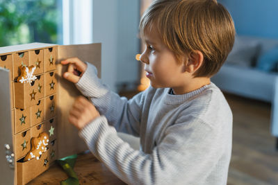 Happy excited little boy opens christmas advent calendar surprise box with gingerbread and sweets.