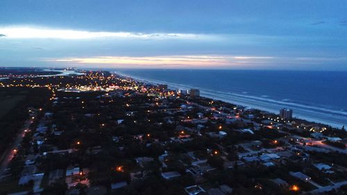 Aerial view of illuminated city by sea against sky