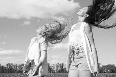 Friends tossing hair while standing against sky