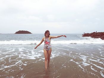 Smiling mid adult woman with arms outstretched standing at beach