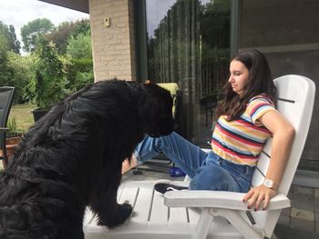 Scared teenage girl looking at black dog on chair outside house