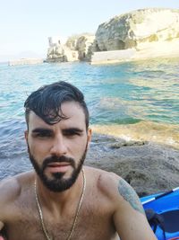 Portrait of shirtless man in sea against sky