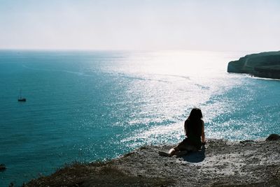 Rear view of woman sitting at beach against clear sky