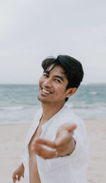 Portrait of smiling man standing at beach against sky