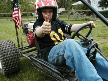 Portrait of boy showing thumbs up while sitting in go-cart