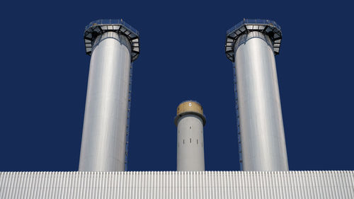 Low angle view of smoke stacks against clear blue sky