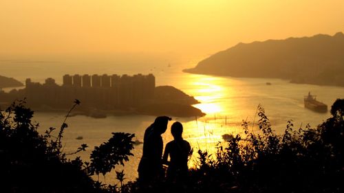 Silhouette couple looking at fort in sea during sunset